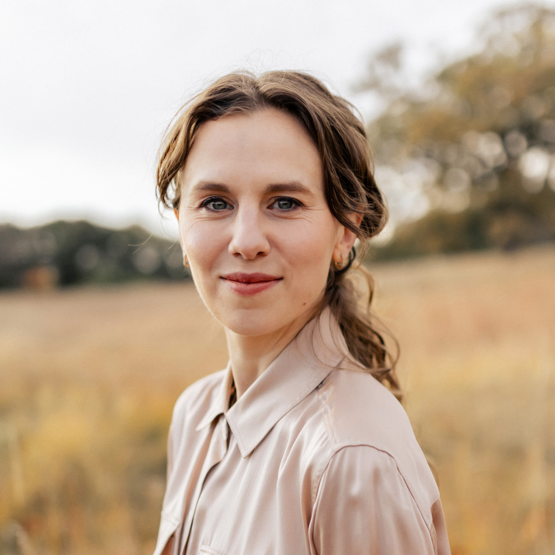 Dasha Gaian standing in a sunlit field wearing a silk shirt